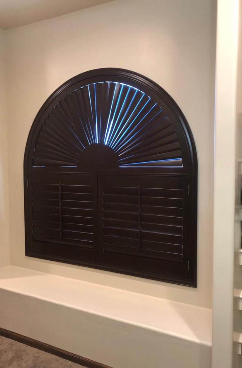 dark stained plantation shutters with an arched sunburst window over a bench nook