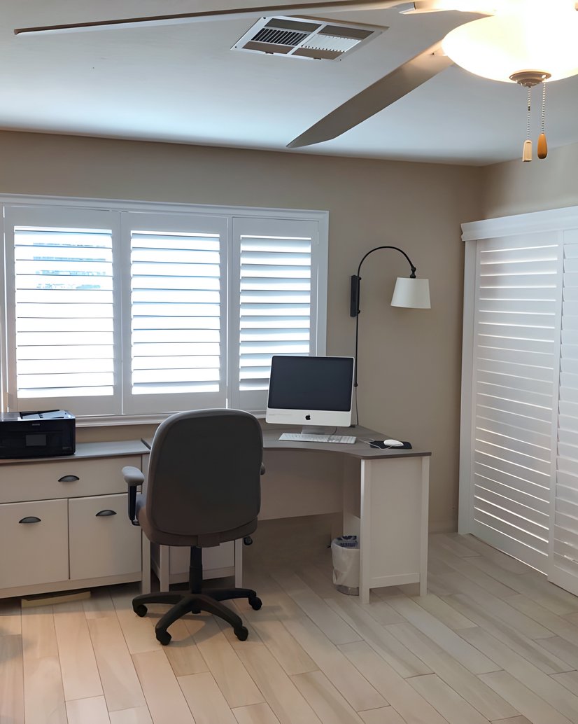 white plantation shutters over a wide window and matching sliding closet shutters in a home office