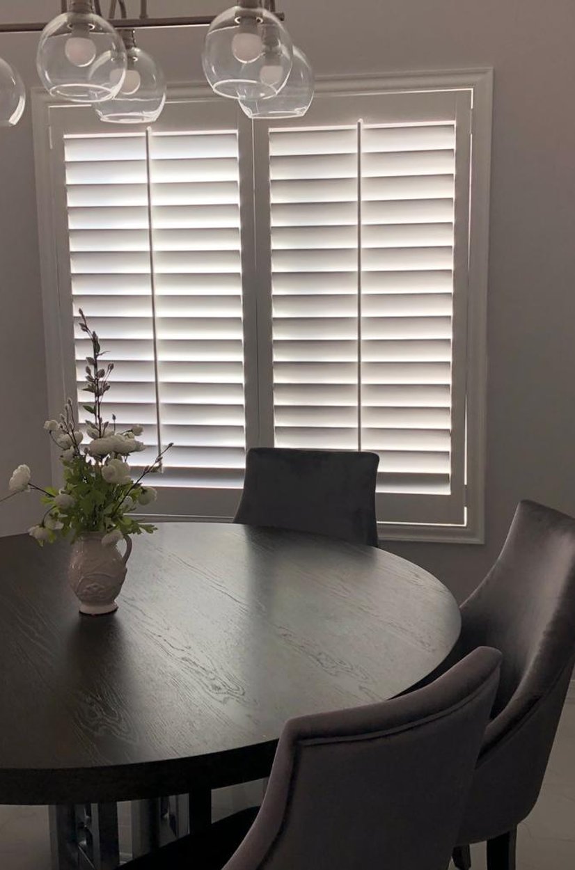 white plantation shutters behind a round dining table