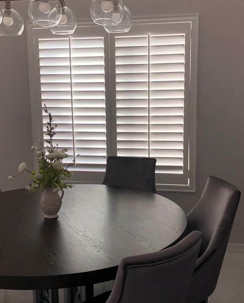 white plantation shutters behind a round dining table